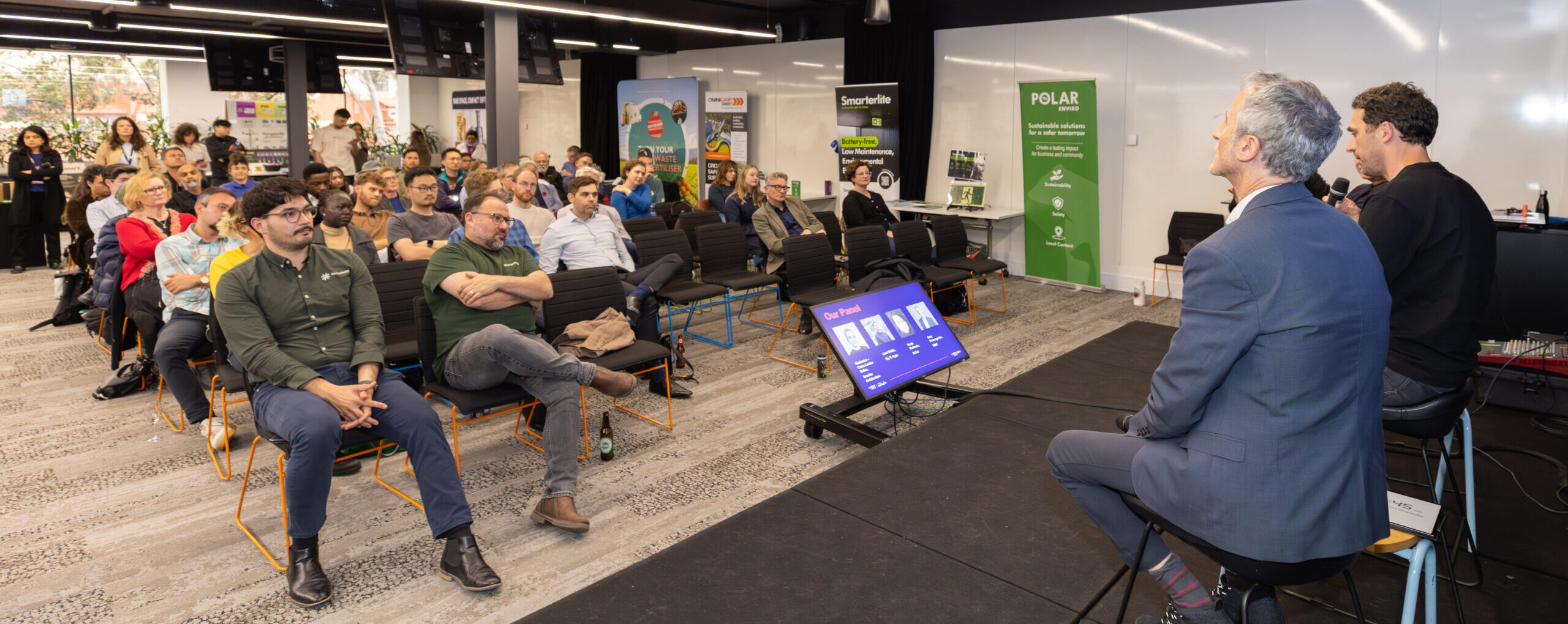 A large group of people are sitting in a room, watching and listening to a presentation. 