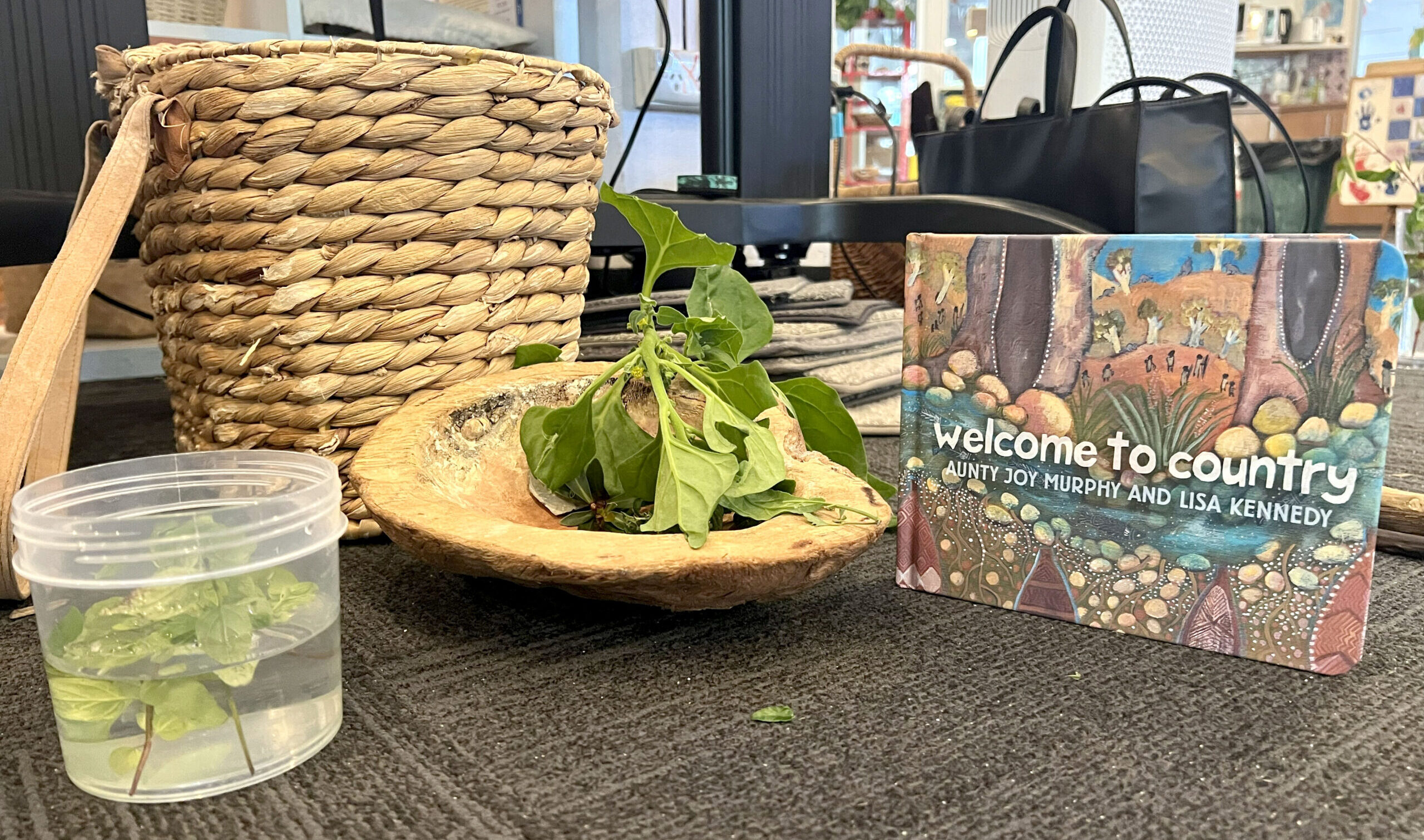 A basket, some leaves in a shell and a book titled "Welcome to Country" sits on a table.