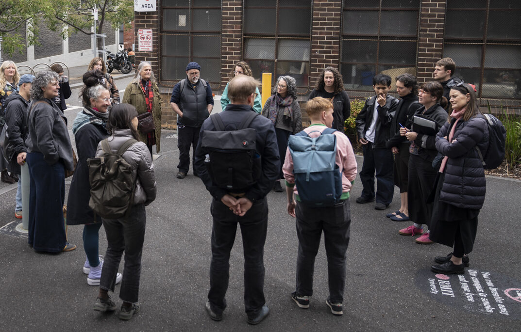 A group of people standing on a street in a circle listening and talking.