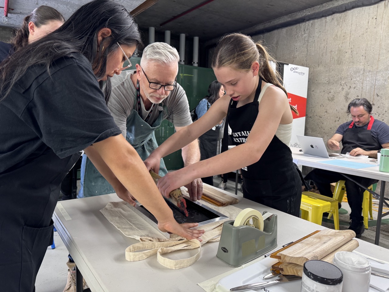 A man, a woman, and a child are working on a table, creating a screen print.