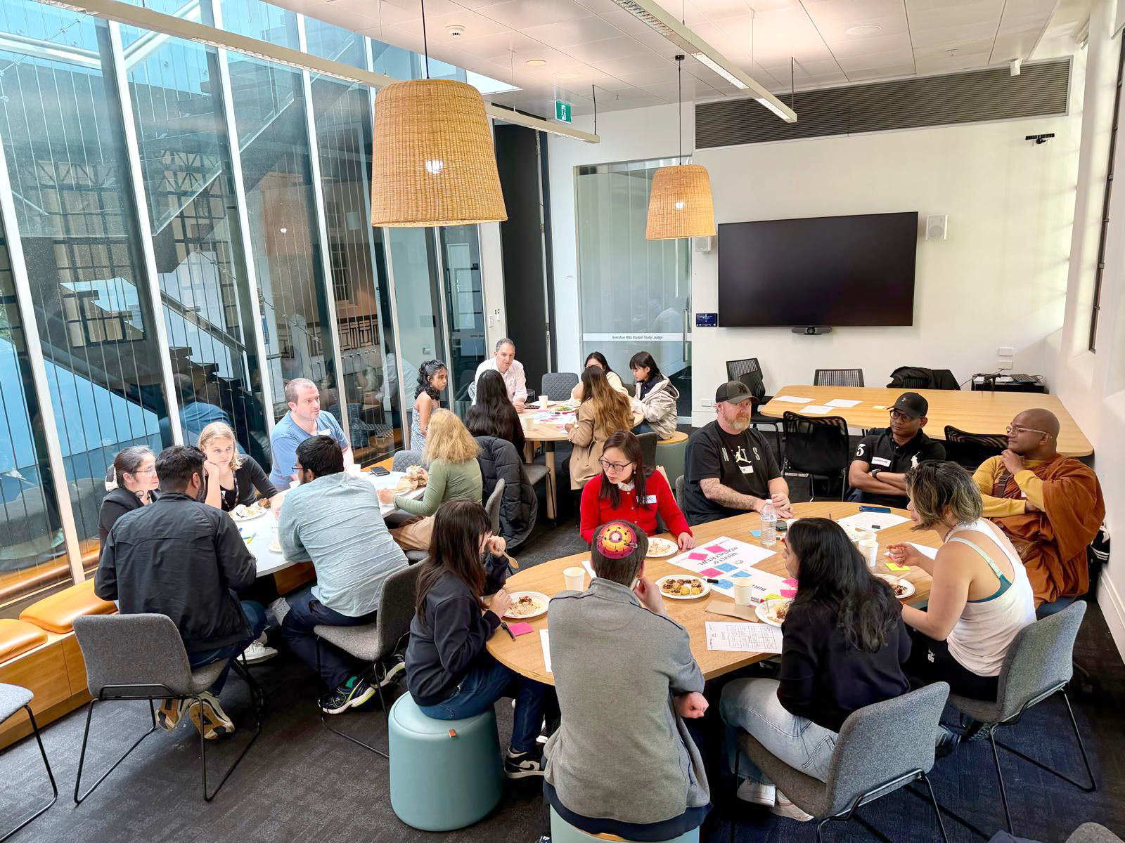 A group of people are sitting around a large table, working on a joint activity in a workshop. There are snacks and drinks on the table and people are engaged in conversation and enjoying their time together.