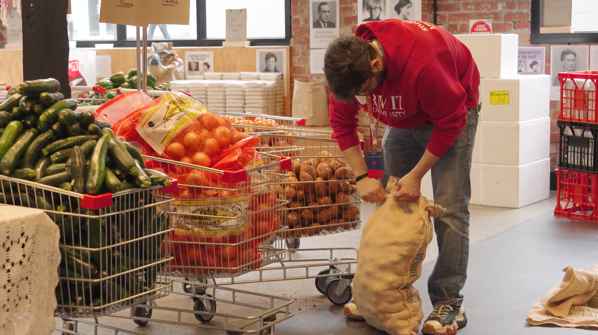A man is bending over, opening a bag of potatoes, with multiple carts next to him, each full of onions and potatoes. 
