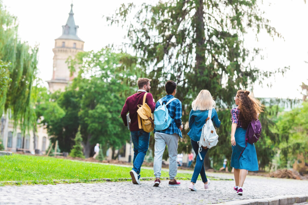 Back view of university students with backpacks walking to campus together.